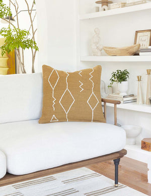 The moroccan ochre and natural beni ourain inspired square flat weave pillow by Sarah Sherman Samuel sits atop a white linen sofa