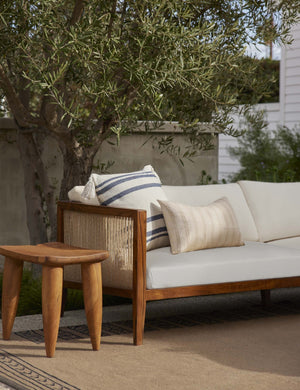 The Fez slate and white indoor and outdoor throw pillow sits on a ivory sofa in an outdoor space on a brown rug