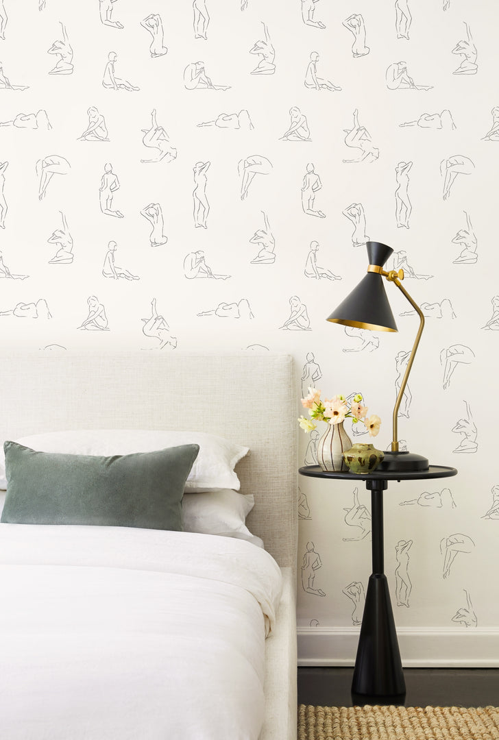 | The Minimalist white and black nude wallpaper is in a bedroom with a gray linen framed bed and a black sculptural nightstand 