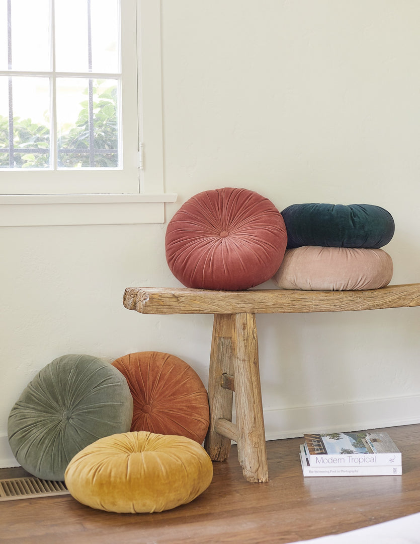 #color::moss #color::rosewater #color::mustard #color::burnt-orange | The Monroe velvet round pillow sits on a wooden bench with other round velvet throw pillows