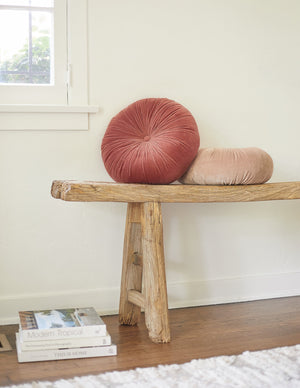 The Monroe coral pink velvet round pillow sits on a wooden bench with the rosewater pink round velvet pillow