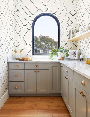 The Moroccan black and ivory Wallpaper Mural by Sarah Sherman Samuel is in a small kitchen with a blue framed window, gray cabinetry, and marbled counter tops.
