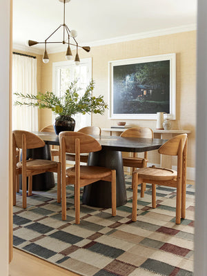 The marli rug lays in a dining room under a rectangular black wooden dining table and sculptural wooden dining chairs