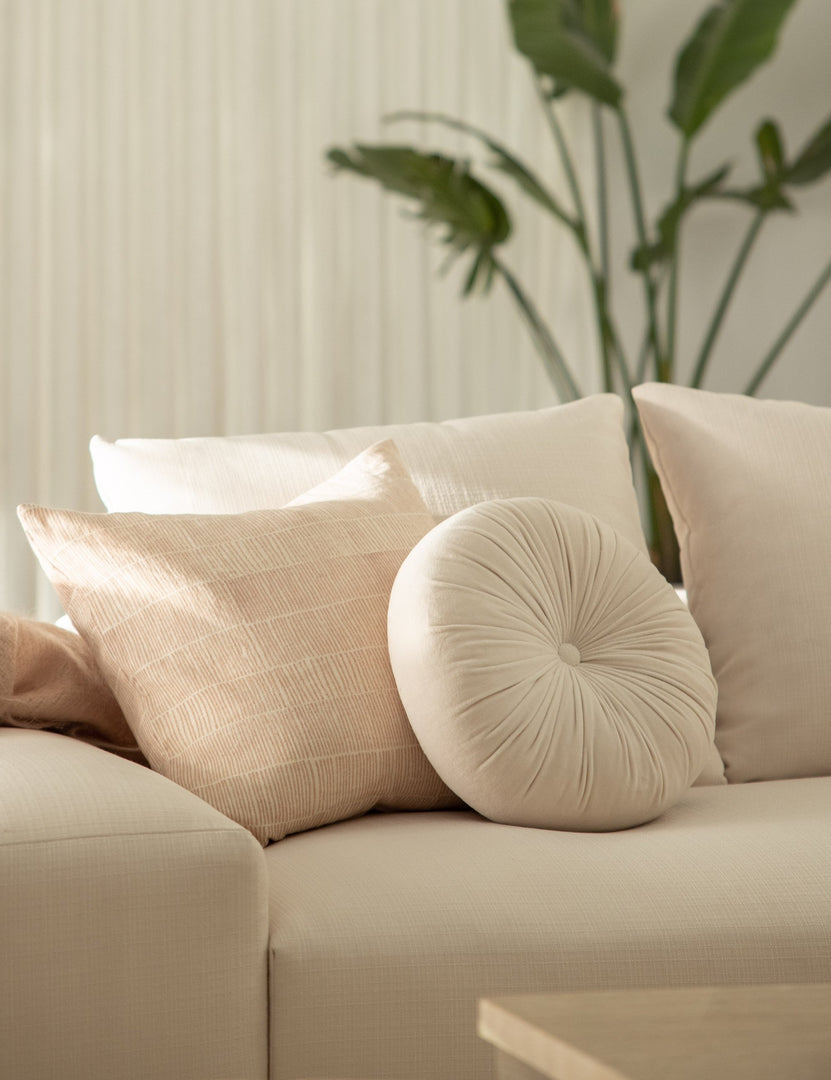 #color::oyster | The Monroe oyster white velvet round pillow sits on a white sofa next to a natural throw pillow