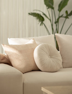 The claudette blush square pillow sits on a natural linen sofa with an oyster velvet disc throw pillow