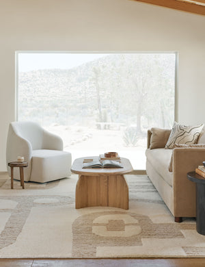 The Tobi natural linen swivel chair sits atop a natural and ivory patterned carpet in front of a large window with a desert view