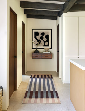 The otti rug in its runner size lays in a hallway that has beamed ceilings, a wooden wall shelf, and an abstract wall art