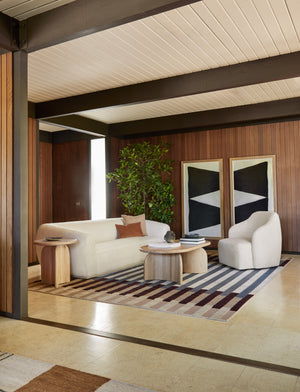 The otti rug lays in a retro living room with wood paneled walls under an oval coffee table and a boucle accent chair