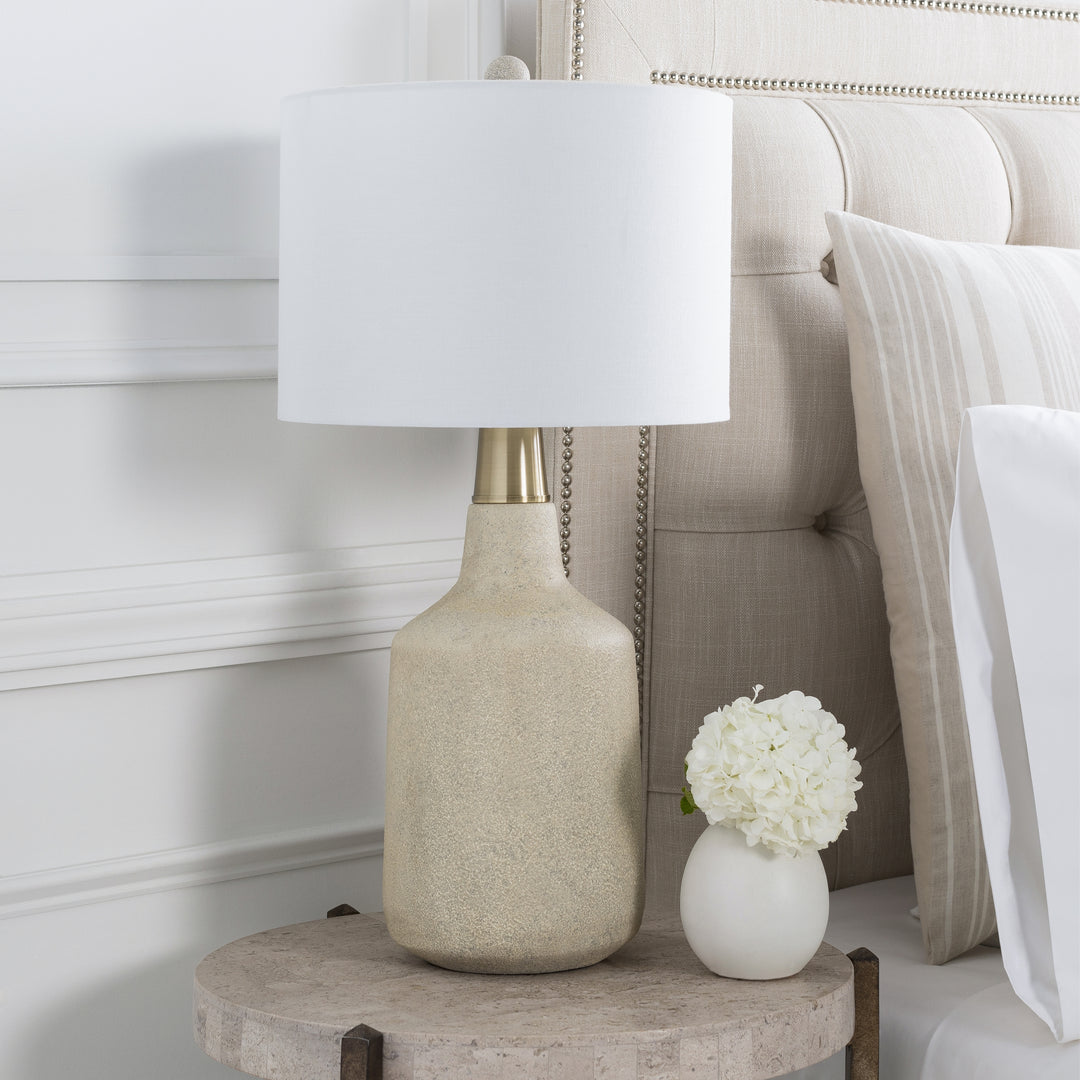 | The Langley table lamp with stone base and white finial sits atop a stone bedside table in a bedroom