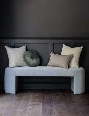 The Manon linen oatmeal cream square boucle pillow sits on a light blue velvet bench with other throw pillows in a room with black accented walls