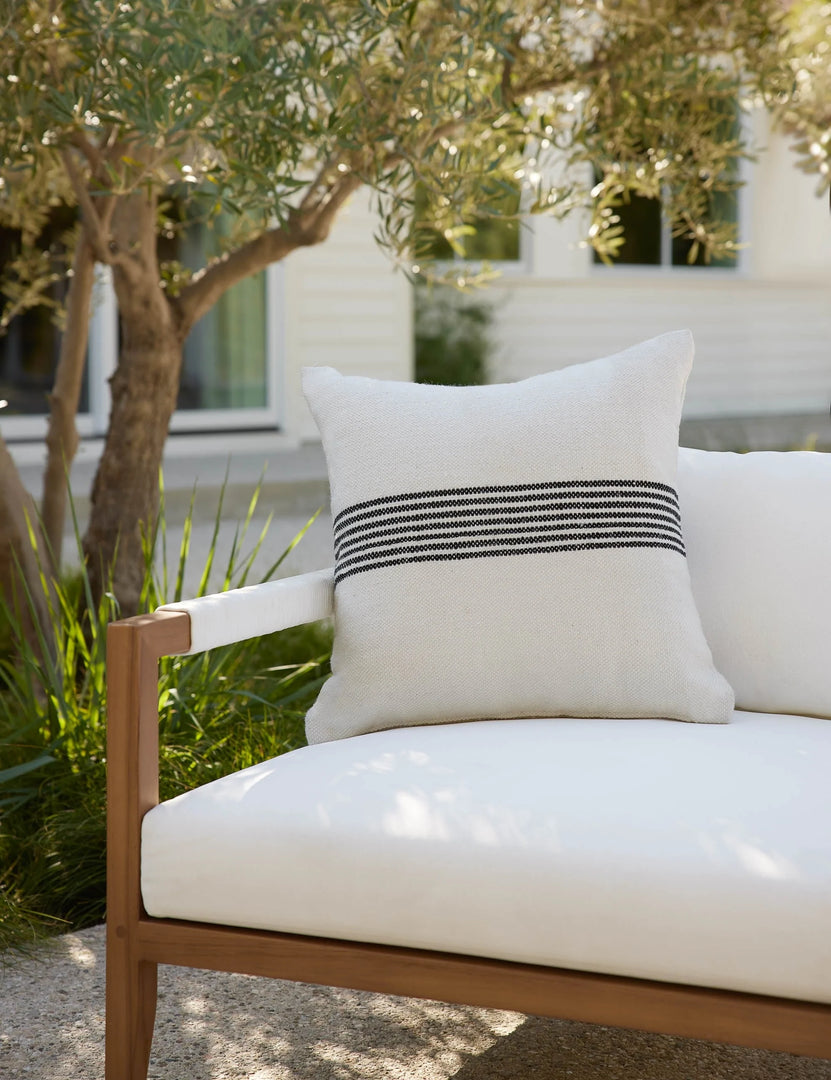 #color::black-stripe #style::square | Katya Indoor and Outdoor square cream Pillow with black stripes in the center sits on a white cushioned sofa in an outdoor space