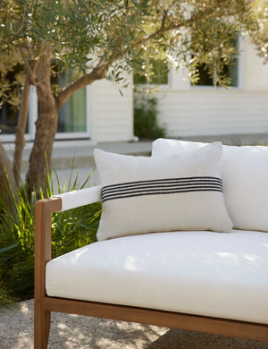 Katya Indoor and Outdoor lumbar cream Pillow with black stripes in the center sits on a white cushioned sofa in an outdoor space