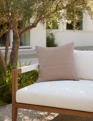 Rust brown Milan indoor and outdoor square pillow with a linear pattern by Sunbrella sits on a white cushioned sofa in an outdoor space