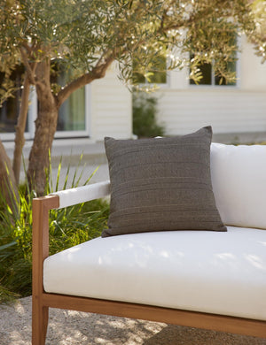 Milan indoor and outdoor square pillow with a linear pattern by Sunbrella sits on a white cushioned sofa in an outdoor space