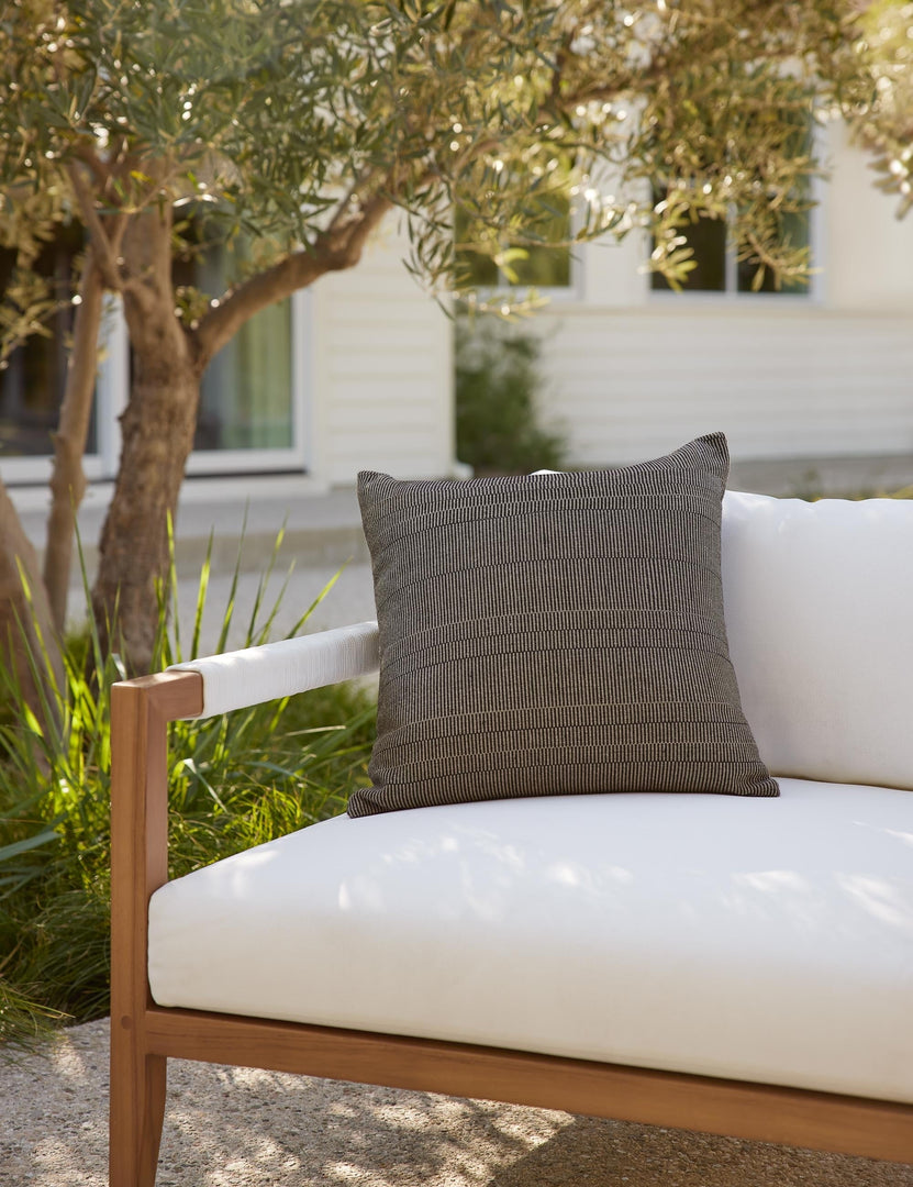 #color::black #style::square | Milan indoor and outdoor square pillow with a linear pattern by Sunbrella sits on a white cushioned sofa in an outdoor space