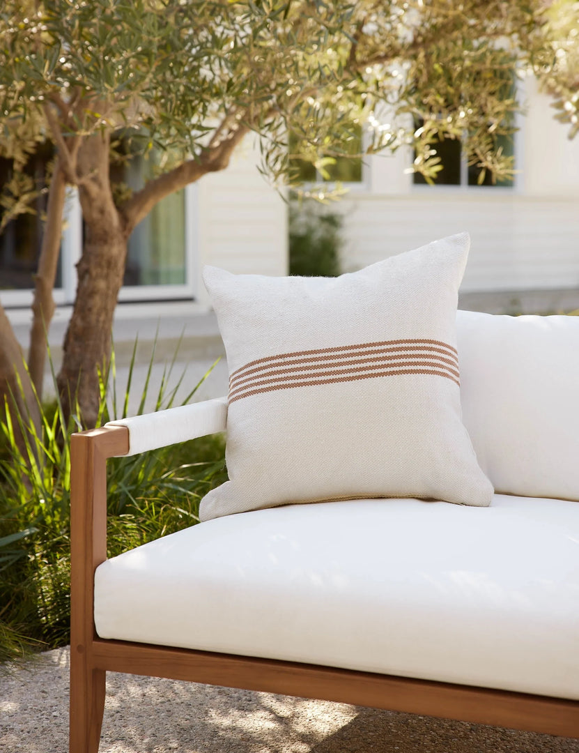 #color::rust-stripe #style::square | Katya Indoor and Outdoor square cream Pillow with rust brown stripes in the center sits on a white cushioned sofa in an outdoor space