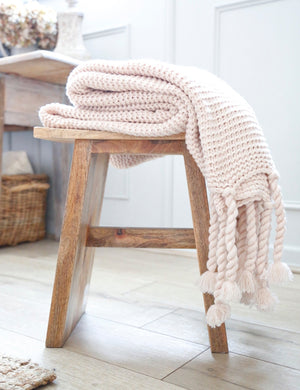 The Trestles blush pink chunky knit throw by pom pom at home lays in a bathroom atop a wooden stool