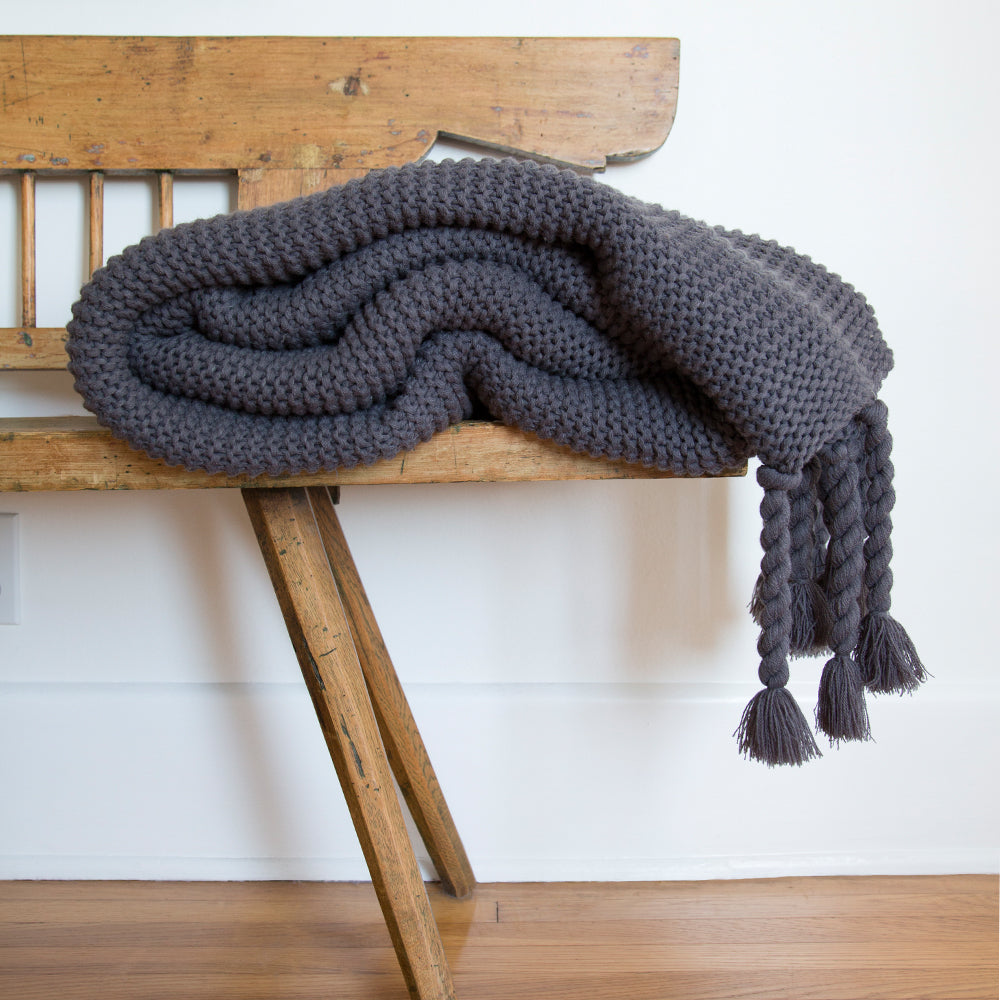 #color::midnight | The Trestles midnight gray chunky knit throw by pom pom at home lays atop a wooden bench