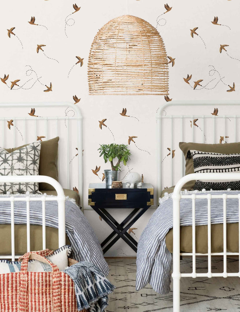 #color::rust | The Sparrow brown wallpaper by Rylee and Cru is in a bedroom with two white victorian style beds with a jute chandelier and black and gold bedside table in the center.