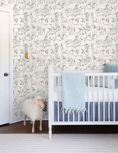| The Woodland Wallpaper by Rylee + Cru is in a children's room with a sheep toy and a white crib with ivory and blue linens