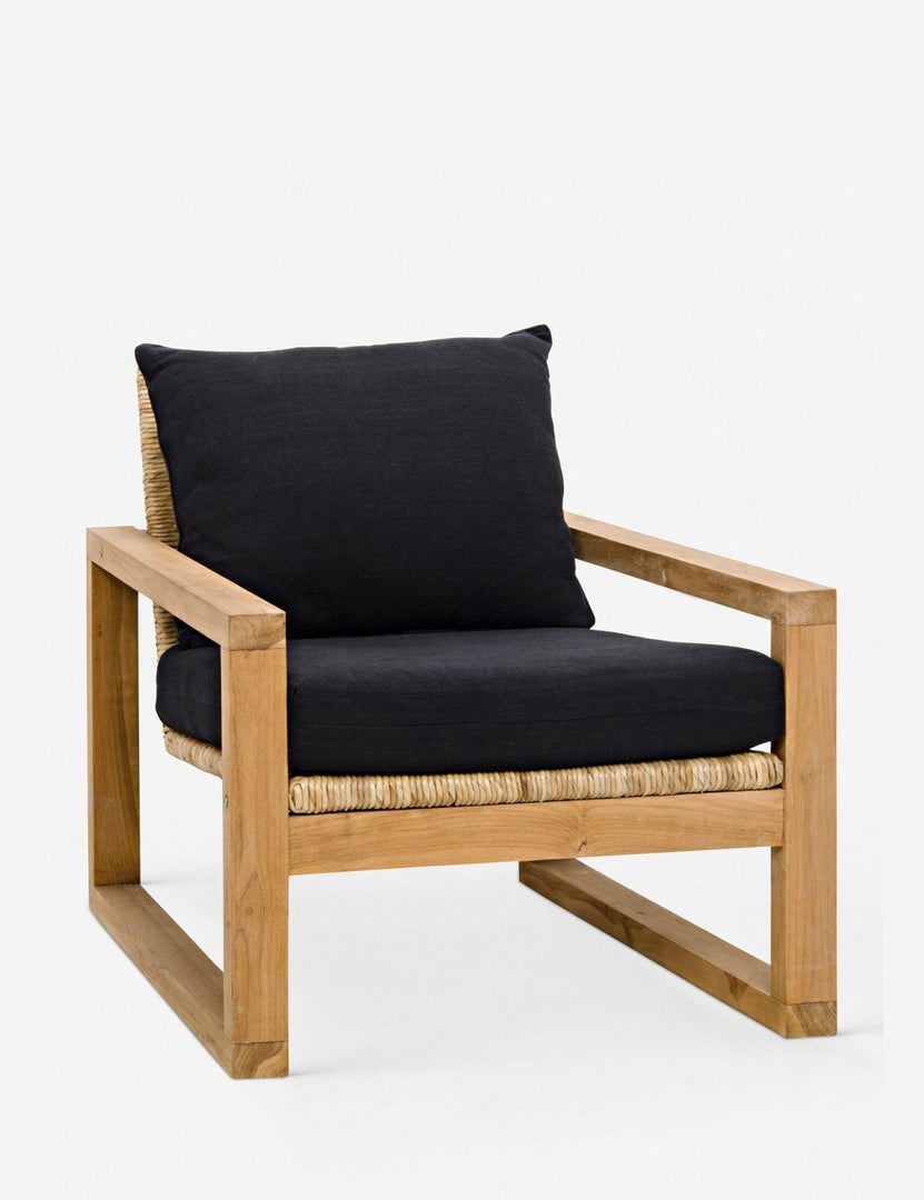| Angled view of the Regine wooden accent chair with black cushions and rattan detailing