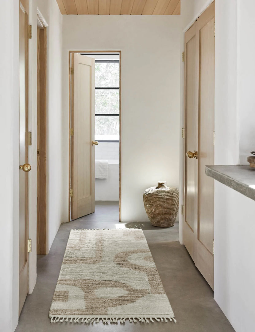#size::2-6--x-8- | The Nomad neutral-toned geometric floor rug by Élan Byrd with subtle ribbed design in its runner size lays in a hallway with a wooden paneled ceiling, a jute basket, and neutral wooden doors with golden knobs