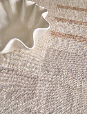 Close-up of the Safi bauhaus-inspired neutral striped area rug with a white ruffle bowl sitting atop it