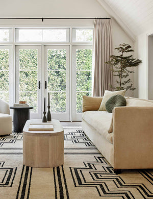 Lotte Camel Velvet Sofa sits in a living room with a wooden oval coffee table and a black and neutral patterned rug