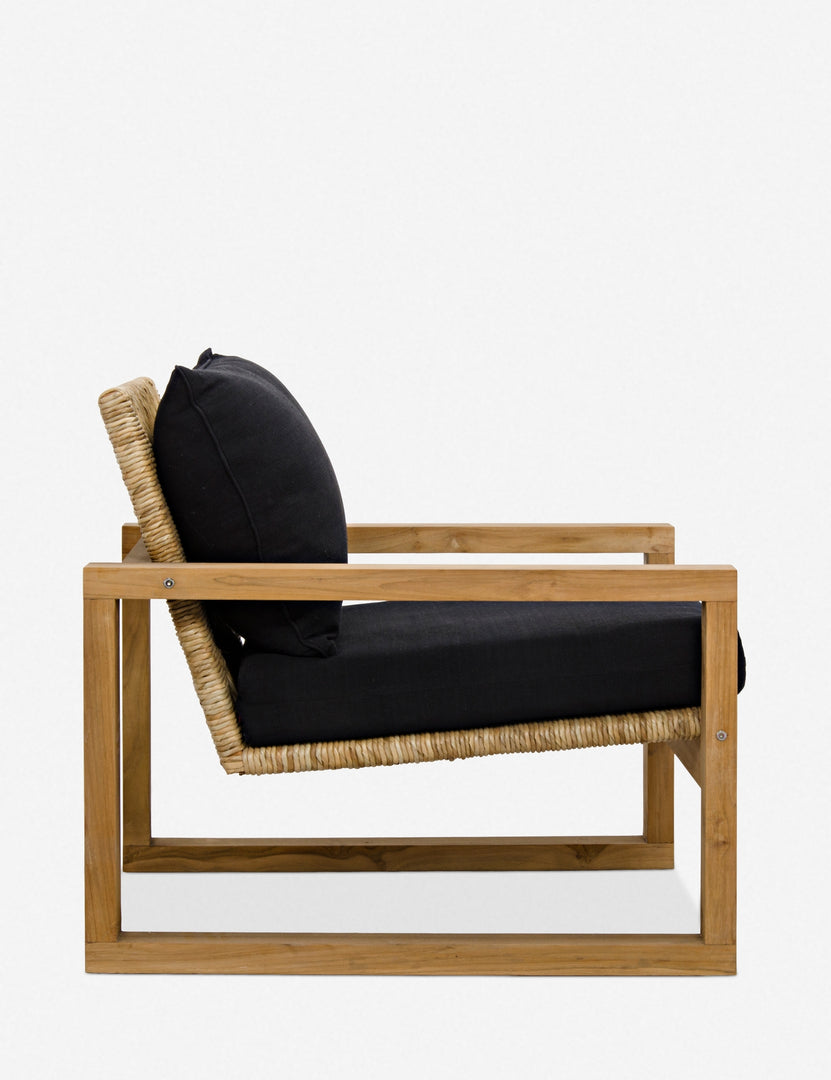 | Side view of the Regine wooden accent chair with black cushions and rattan detailing