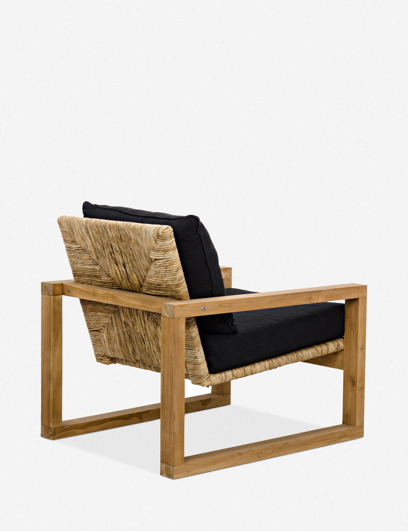 | Angled rear view of the Regine wooden accent chair with black cushions and rattan detailing, showing the woven cane and rattan detailing on the back of the chair