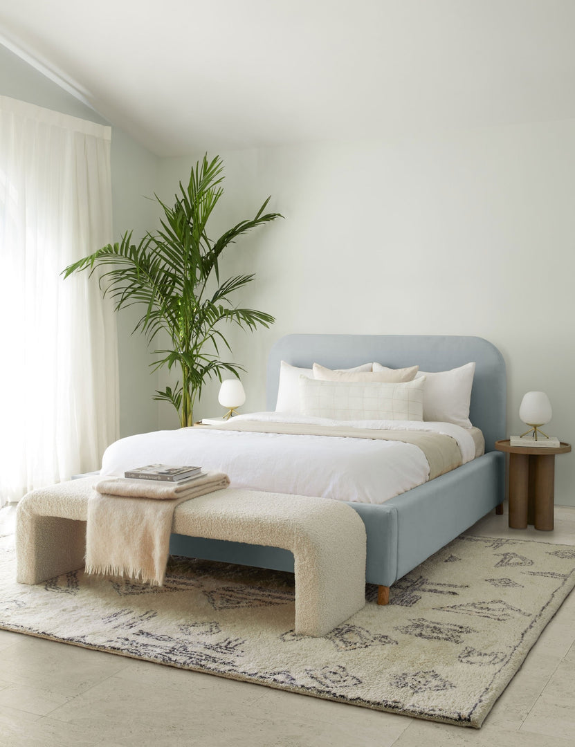 #size::queen #size::king #color::dove #size::cal-king | The Solene dove light blue velvet platform bed sits atop a plush patterned rug with a boucle cream bench and white linens