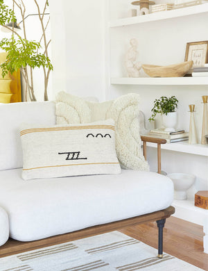 The Iconic ivory stripe lumbar pillow sits on a white sofa with a wood frame with a plush ivory square pillow