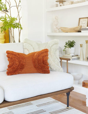 The arches rust lumbar pillow sits with another decorative throw pillow atop a white linen sofa with a wooden frame