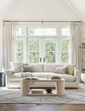 The Walden white sofa sits atop a black and white textured rug behind a white-washed oval coffee table
