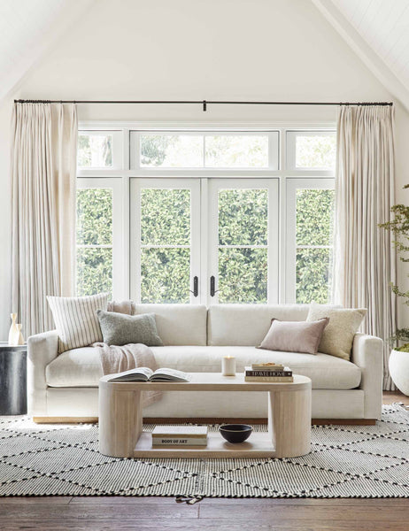 | The Walden white sofa sits atop a black and white textured rug behind a white-washed oval coffee table