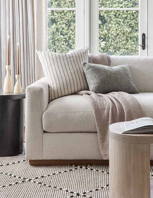 The Manon linen slate gray lumbar boucle pillow sits on a gray linen sofa with other throw pillows in a living room with a black and white rug