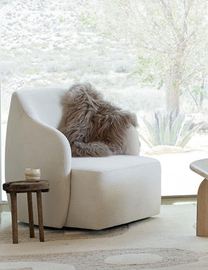 The Vale icelandic light gray sheepskin is laid in a living room atop a white accent chair with a wooden stool and coffee table