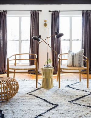 The Leila Moroccan Shag Rug lays in a room in front of two tall windows and under two woven accent chairs and coffee table