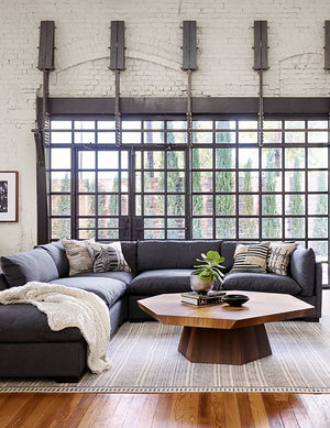 The Balen coffee table sits in a living room with large windows atop a gray rug and next to a dark blue sectional