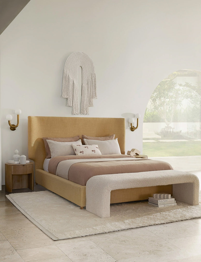 #size::queen #size::king #color::wheat #size::cal-king | The Valen wheat linen platform bed sits atop a plush ivory rug with dusty pink and white linens in between two brass sconce lights