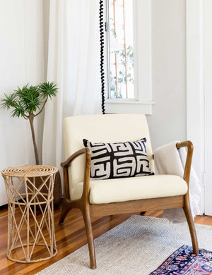 The Venturi white upholstered accent chair sits in the corner of a room with a sculptural woven side table, a black and white patterned throw pillow, and layered rugs.